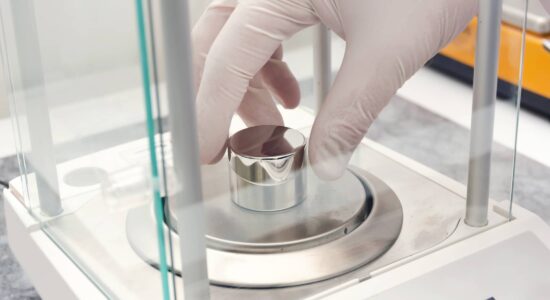 A person wearing gloves places a sample container on a laboratory balance